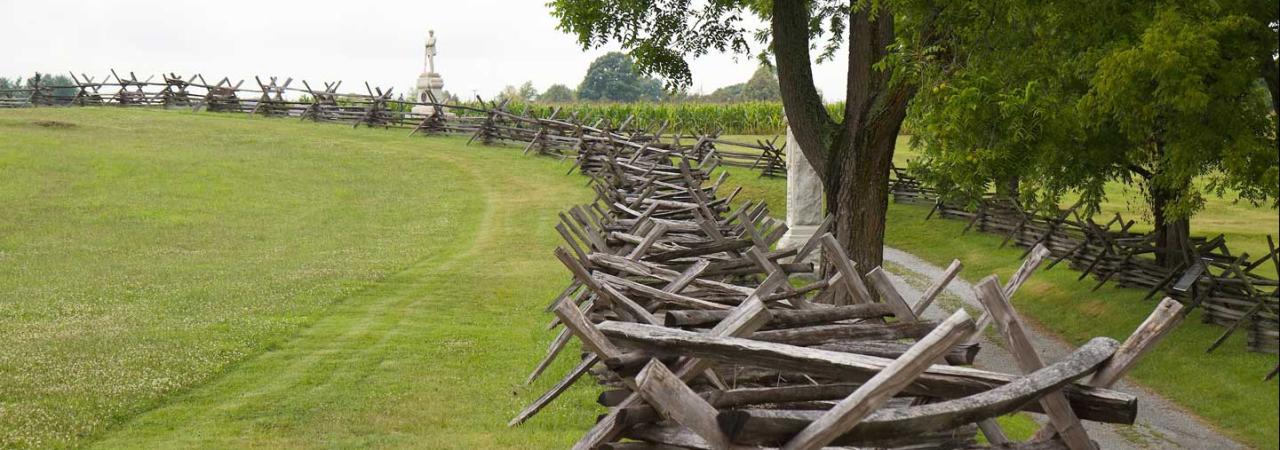 A split rail fence at Antietam National Battlefield. A statue is in the distance, a tree in the forground.