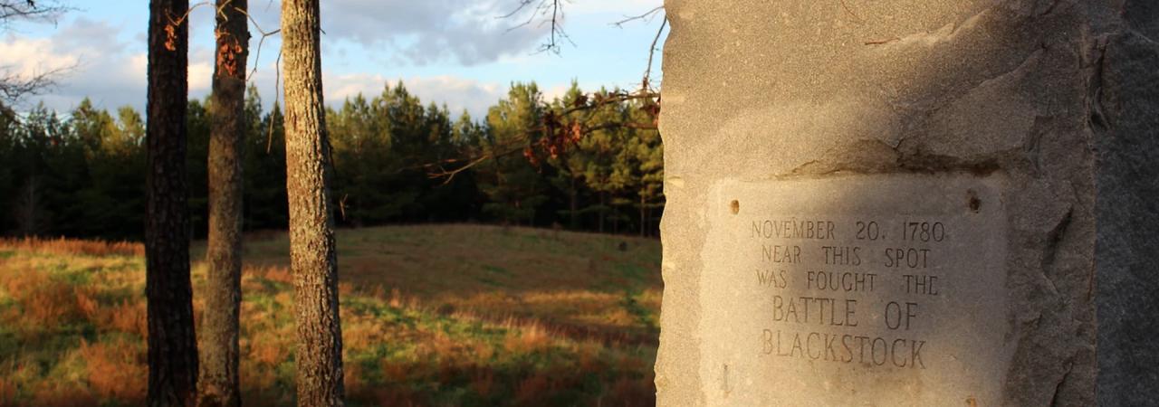 Photograph of a battlefield with a stone marker in the foreground. 