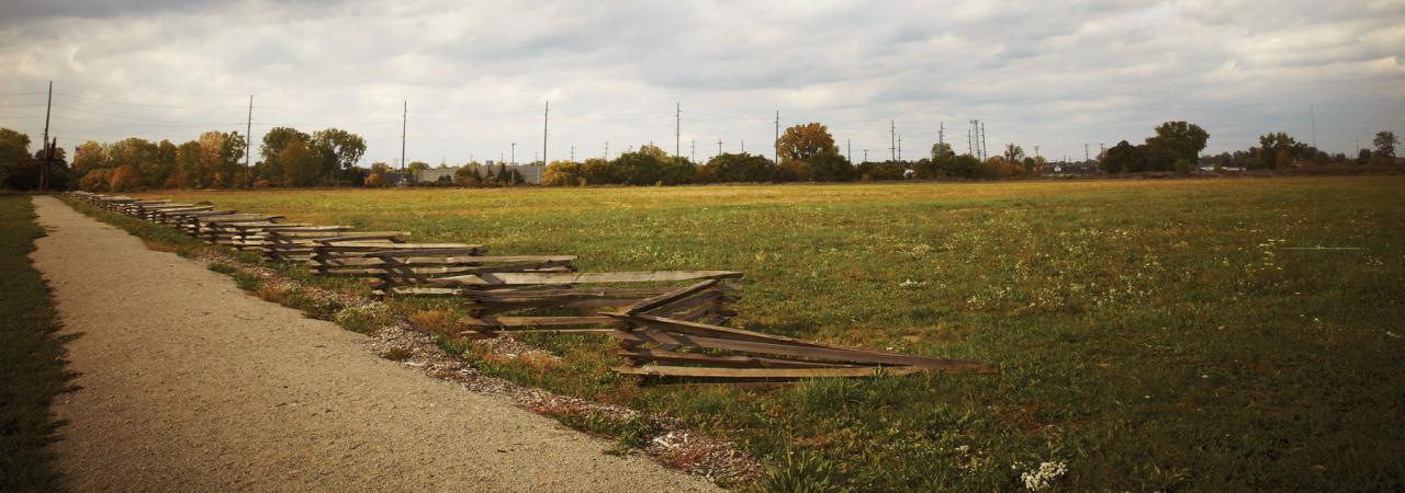 Snake Rail Fence with a dirt road and field, with a full sky of puffy white clouds 