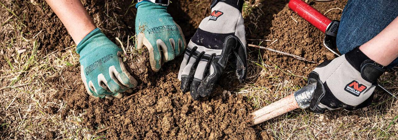 Archeologists digging in the earth with gloved hands and tools.