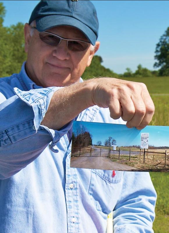 Historian Bud Hall holds a picture of the "for sale" signs and development proposals that once threatened the land where he's standing, now owned by the Trust.