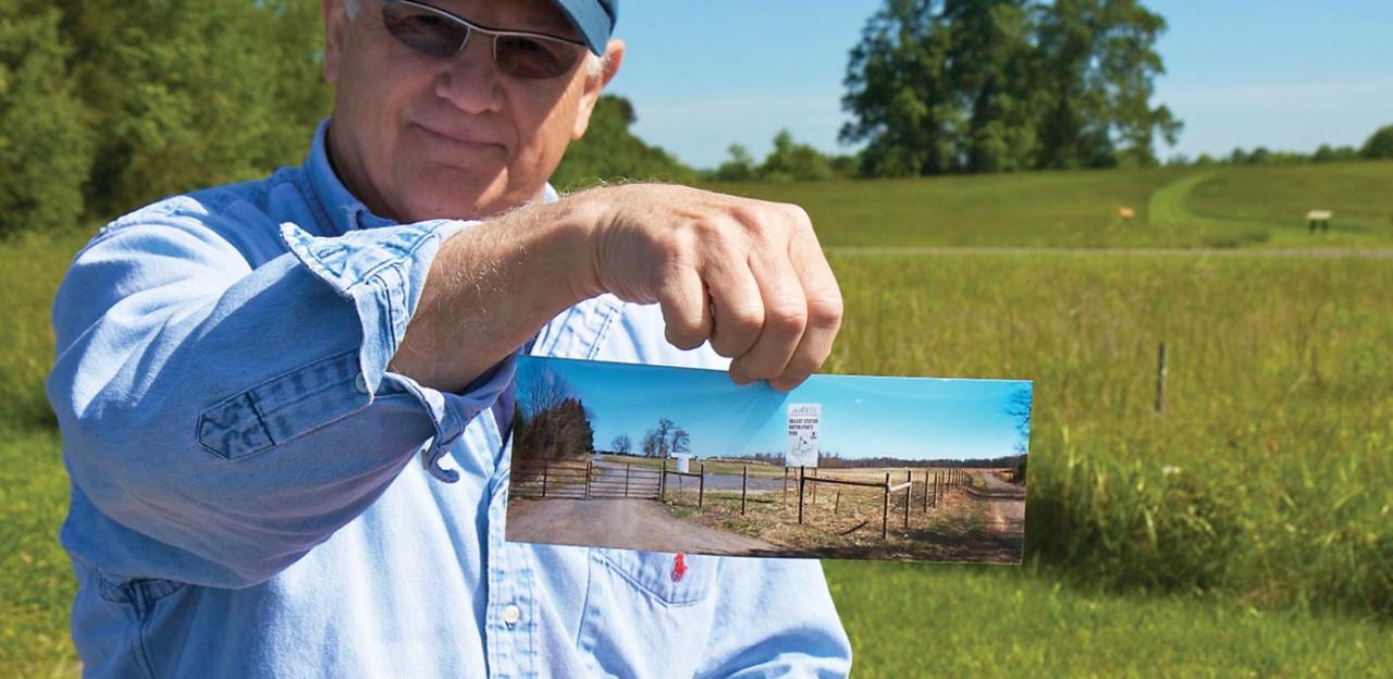 Historian Bud Hall holds a picture of the "for sale" signs and development proposals that once threatened the land where he's standing, now owned by the Trust.