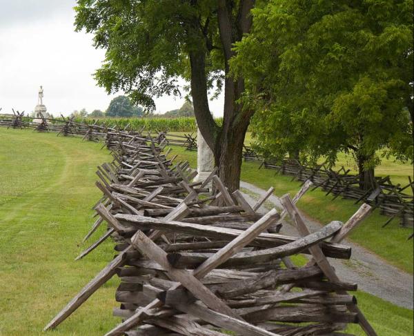 A split rail fence at Antietam National Battlefield. A statue is in the distance, a tree in the forground.