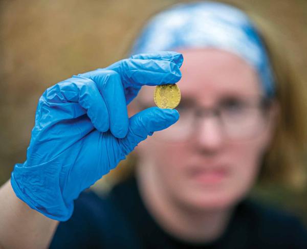 History professor Jennifer Janofsky holds a rare 1766 King George III gold guinea, the equivalent of a soldier’s wages for a month, found during the excavation.