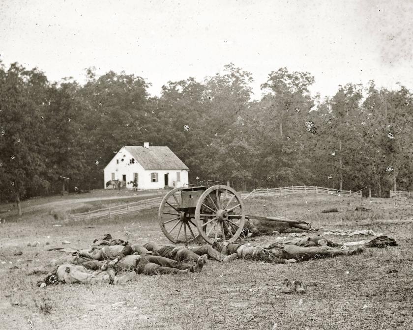 A black and white photograph of Dunker Church with Confederate Dead and a cannon in the foreground.