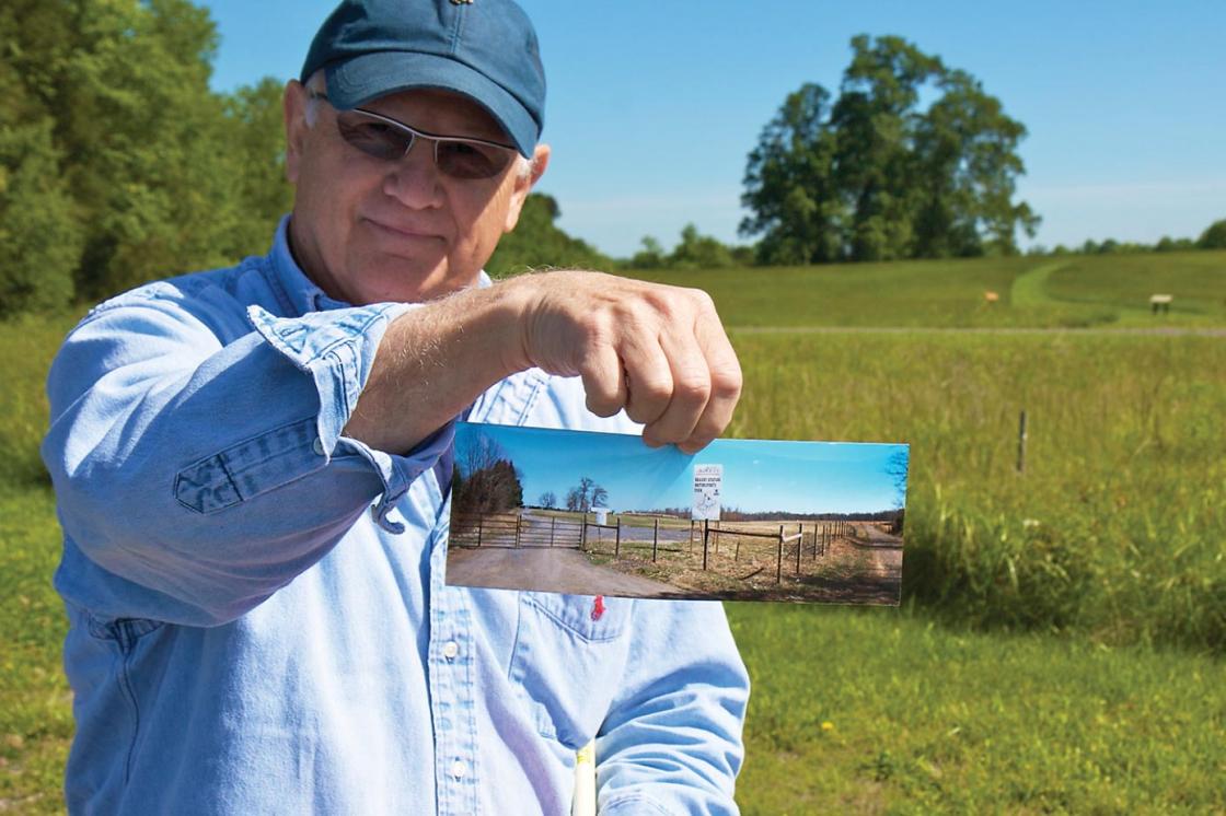 Historian Bud Hall holds a picture of the "for sale" signs and development proposals that once threatened the land where he's standing, now owned by the Trust.