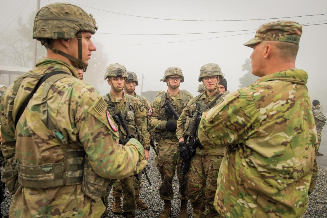 Group of less than 10 cadets in fatigues huddle in discussion